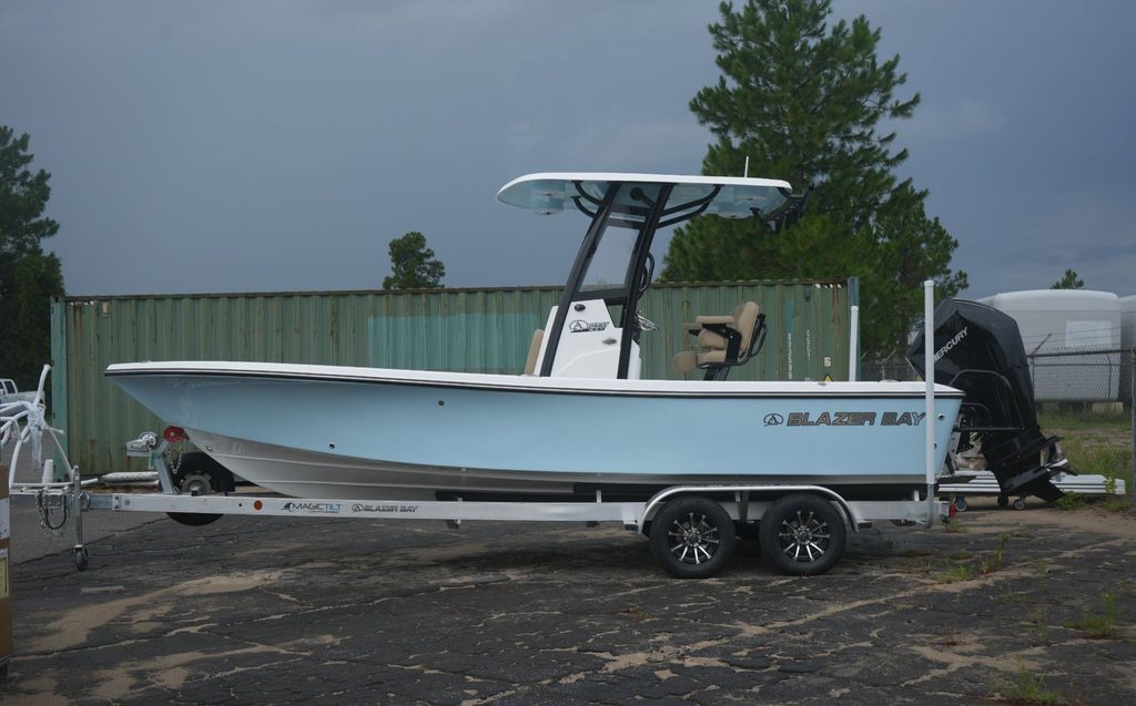 Blazer Bay 2440 with a hard top. The boat is on a trailer in a parking lot in front of a shipping container and some trees.