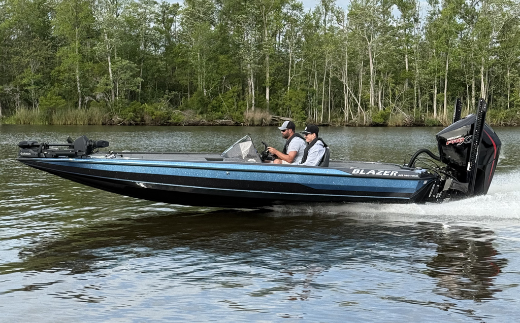 A 625 Pro Tour driving down a river with a forest in the background. There are two men in the main seats of the boat facing forward.