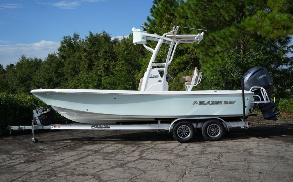 A Blazer Bay 2440 with a half tower second station. The boat is on a trailer in a parking lot in front of a forest.